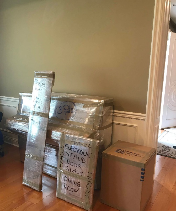 Household furniture wrapped in protective plastic and hand-labeled by room and contents, marked fragile, before a Presto Movers residential move
