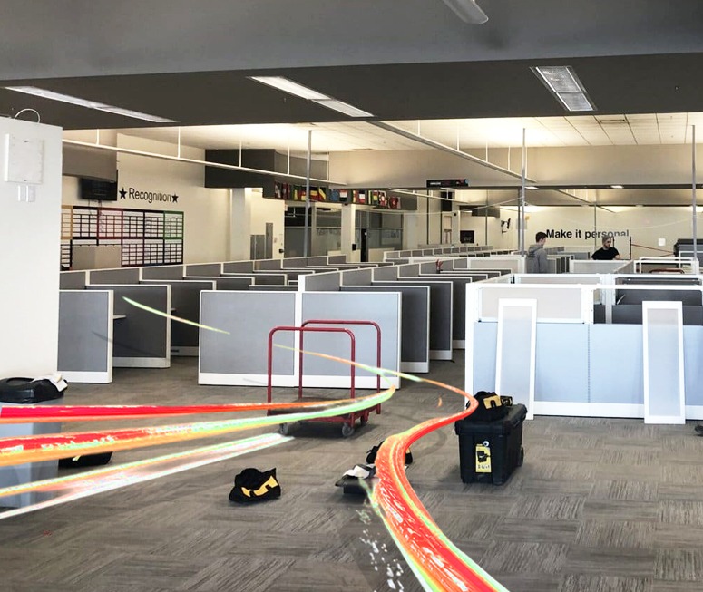 An office floor mid-clearance, with cubicle panels detached and stacked and tool bags on the carpet